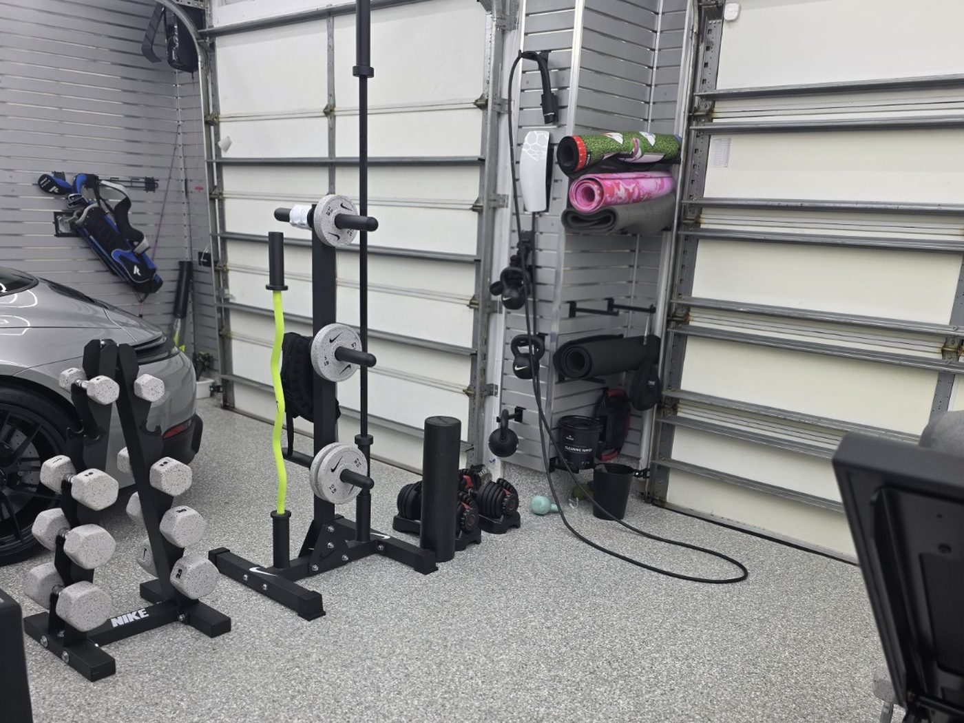 Dumbbell rack, plate tree and loaded bar against the garage bay wall on epoxy flooring