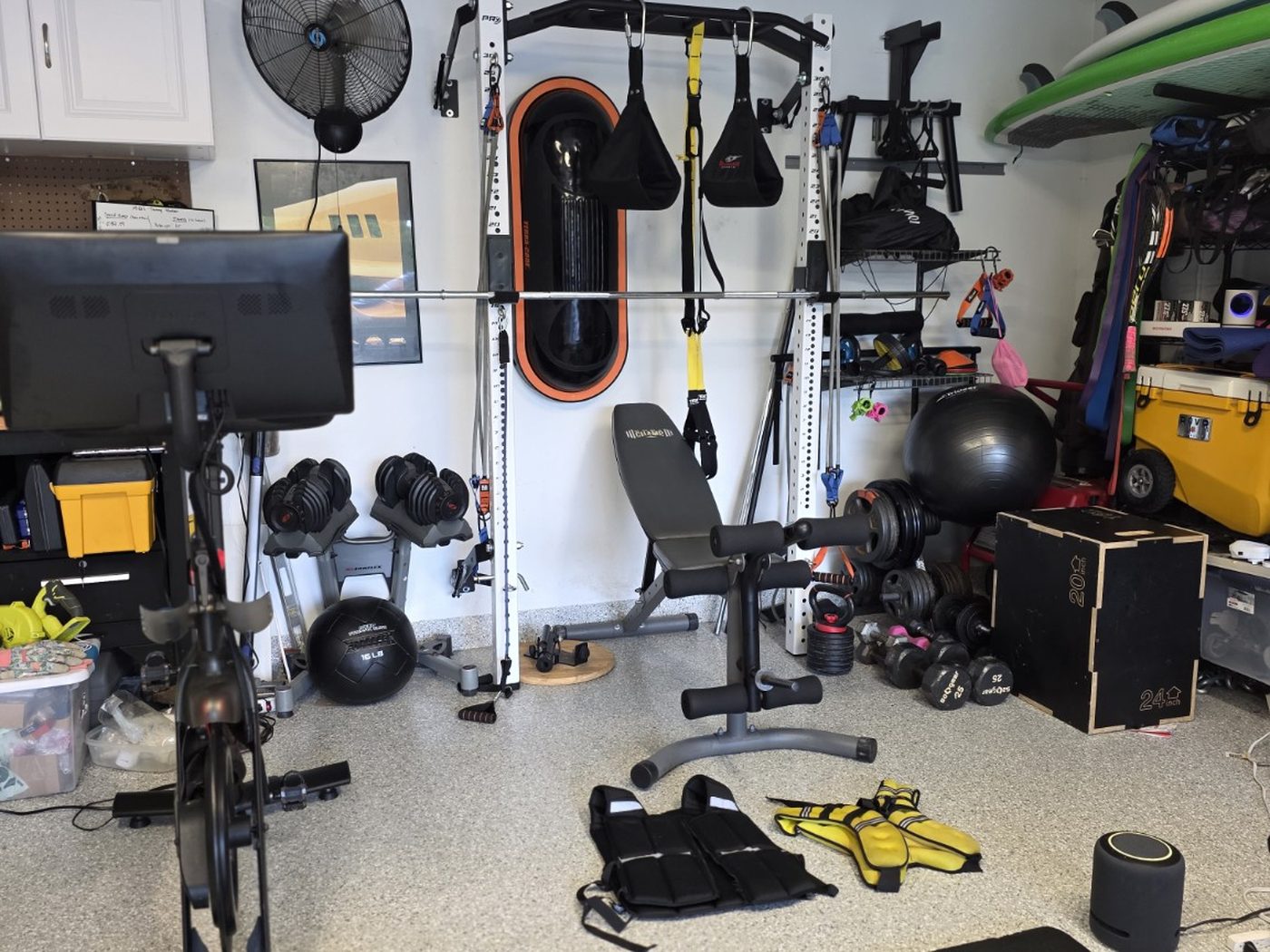 Wider view of the shared garage gym with bike, bench, plyo boxes and overhead storage for surfboards