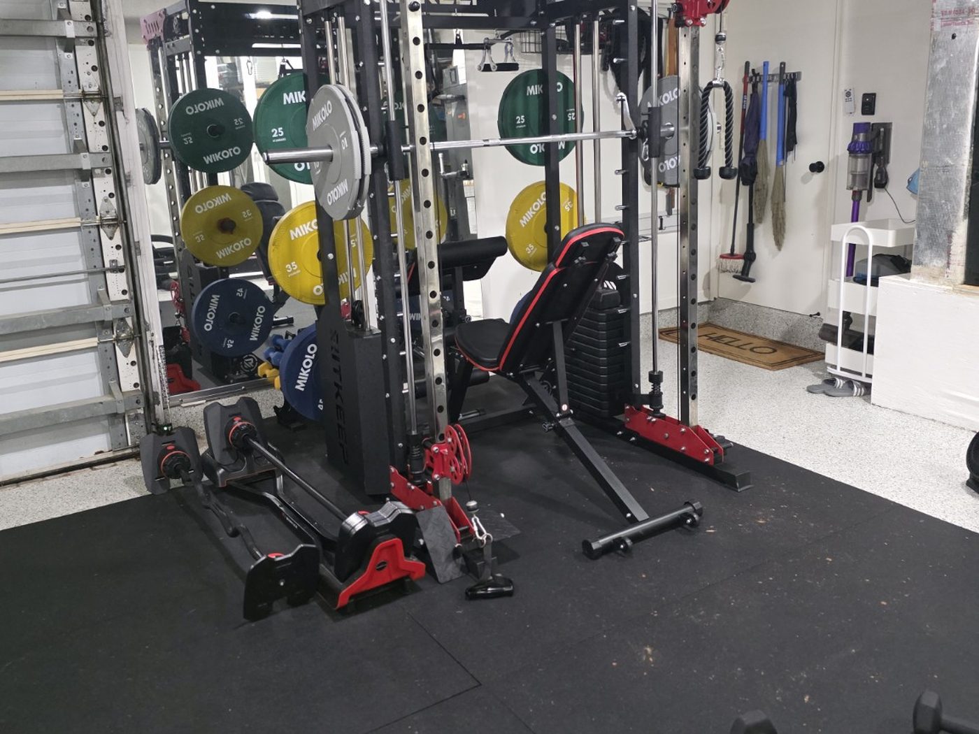 Angled view of the functional trainer showing the mirror, bench and wall-hung cleaning and training attachments